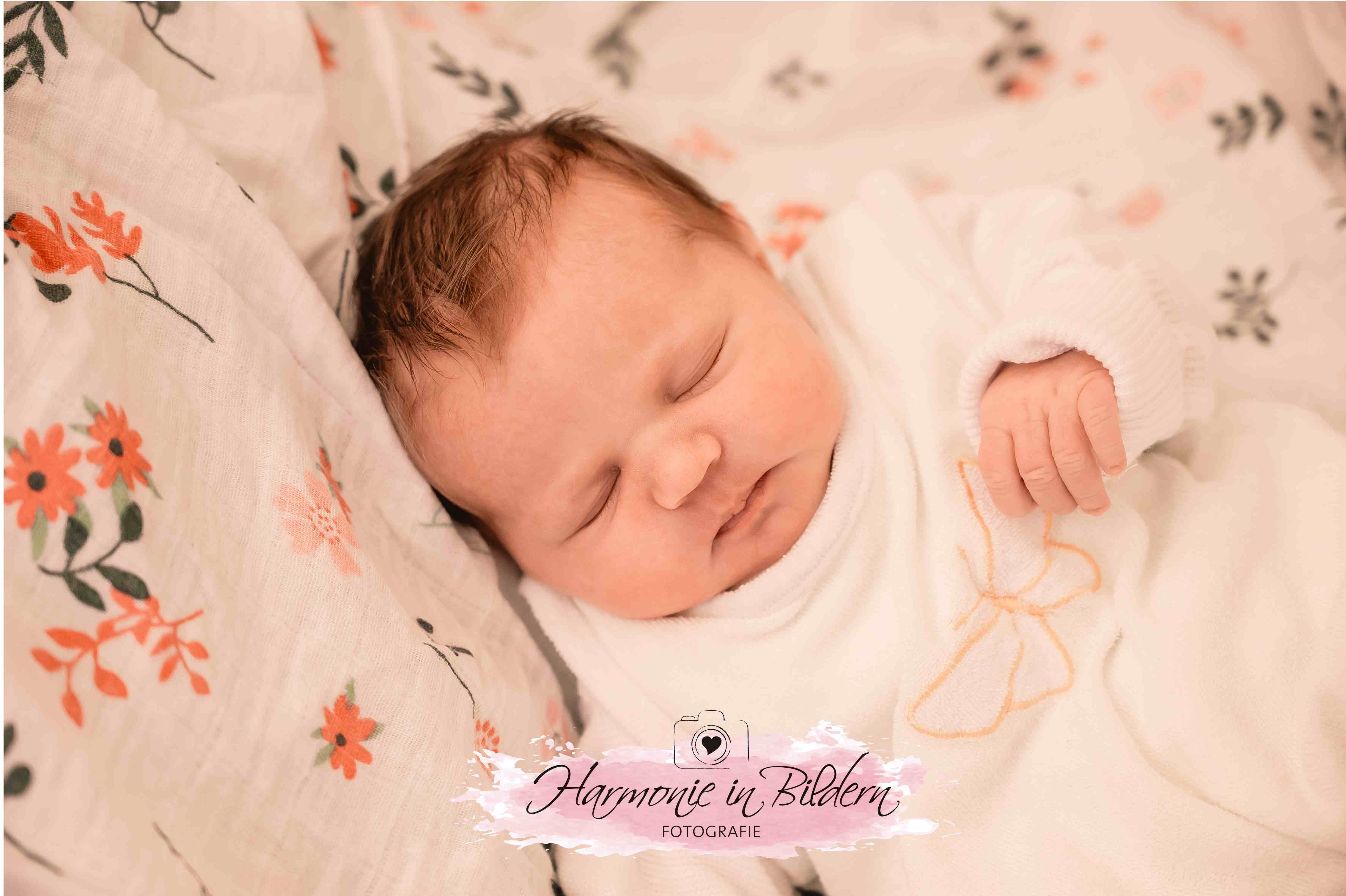 Neugeborenes Mädchenmit dunklen Haaren auf Blumendecke