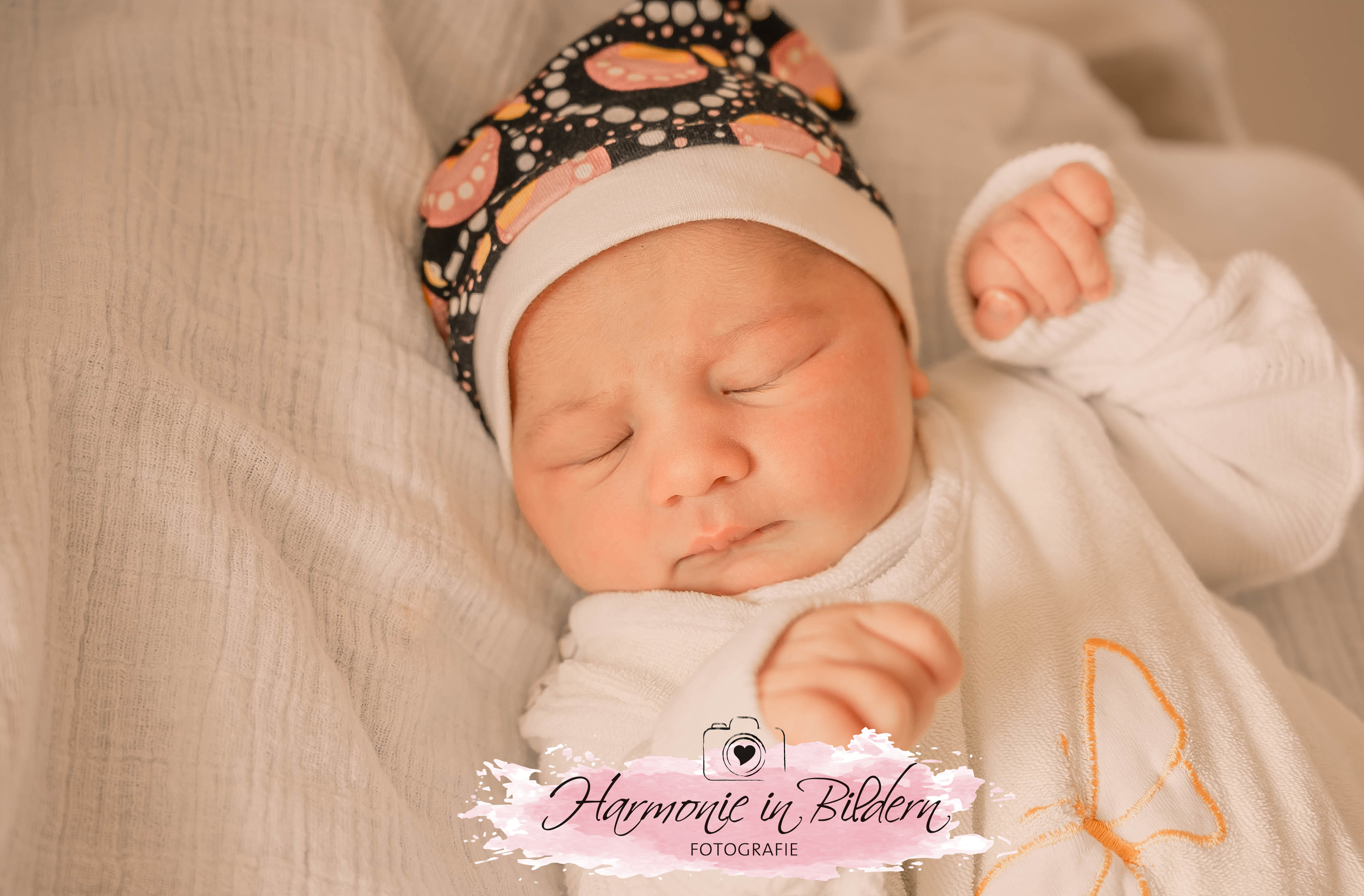 Baby Mädchen auf weisser Decke mit dunkler Mütze
