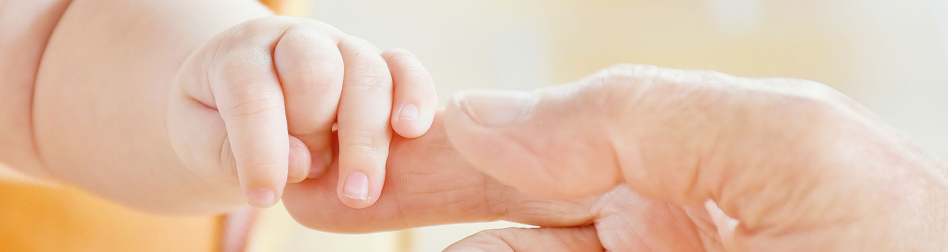 Eine Babyhand greift nach den Fingern des Vaters