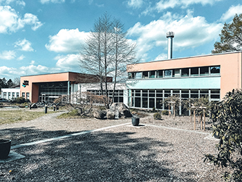 Foto eines Gebäudes mit Schornstein und einem großem Vorplatz.