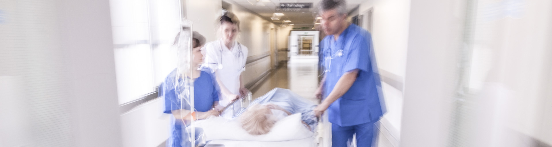 Medizinisches Personal schiebt einen Patienten im Bett über den Flur.